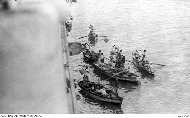 Local men trading with troops on board an Australian transport at the port of Aden, Egypt. Baskets transferring food and goods are being lifted up to the ship by a set of ropes. Australian War Memorial collection C02540