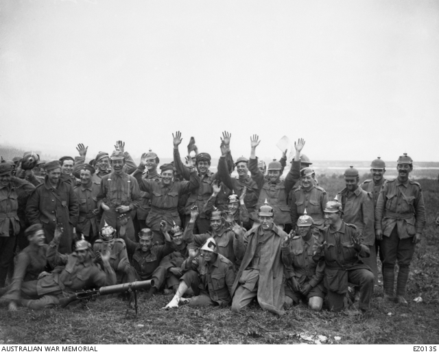 Informal group portrait of unidentified Australian soldiers sporting helmets (Pickelhauben) and caps captured from the Germans in the battle of Pozieres. Some have their hands raised, possibly in a feigned gesture of surrender. In the front on the ground is a Lewis gun. Australian War Memorial collection EZ0135