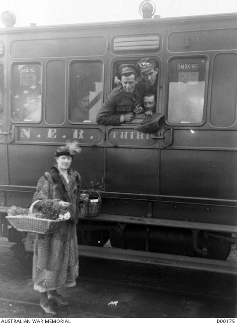A lady worker of the Victorian League stands on the platform with two buckets, distributing fruit and cigarettes through an open window in the train carriage. The returned Australian prisoners of war entrained at Hull, for the receiving camp at Ripon, in England. Australian War Memorial collection D00175